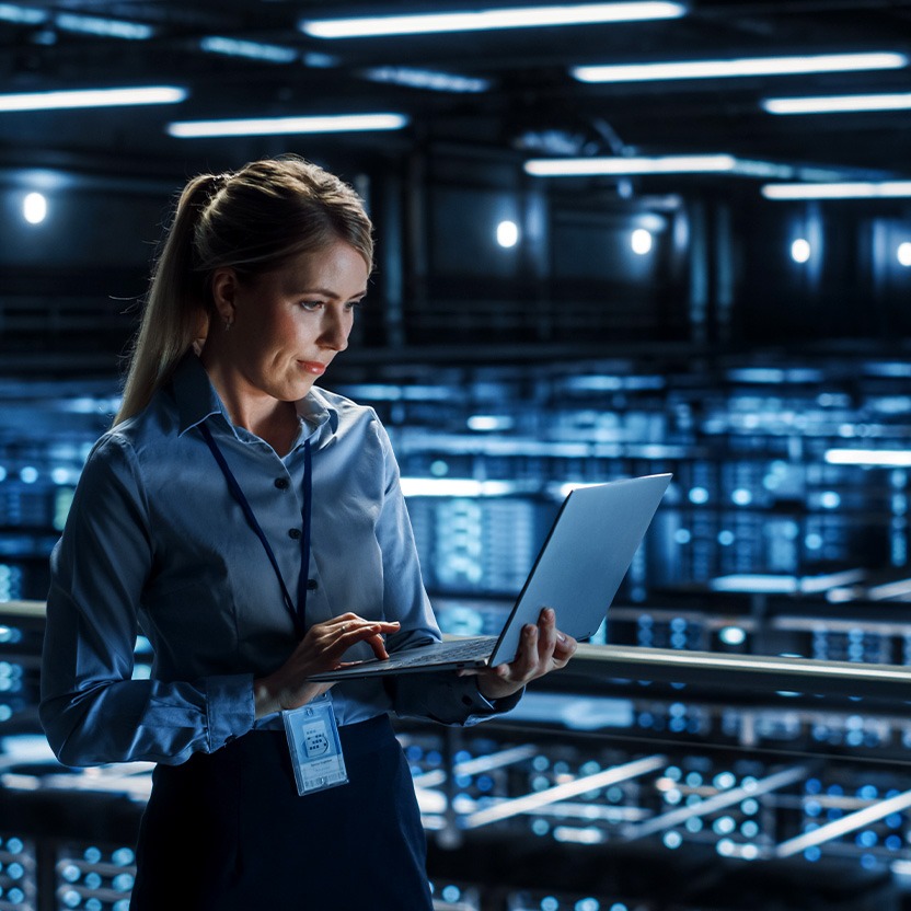 A person in a server room looking at a laptop